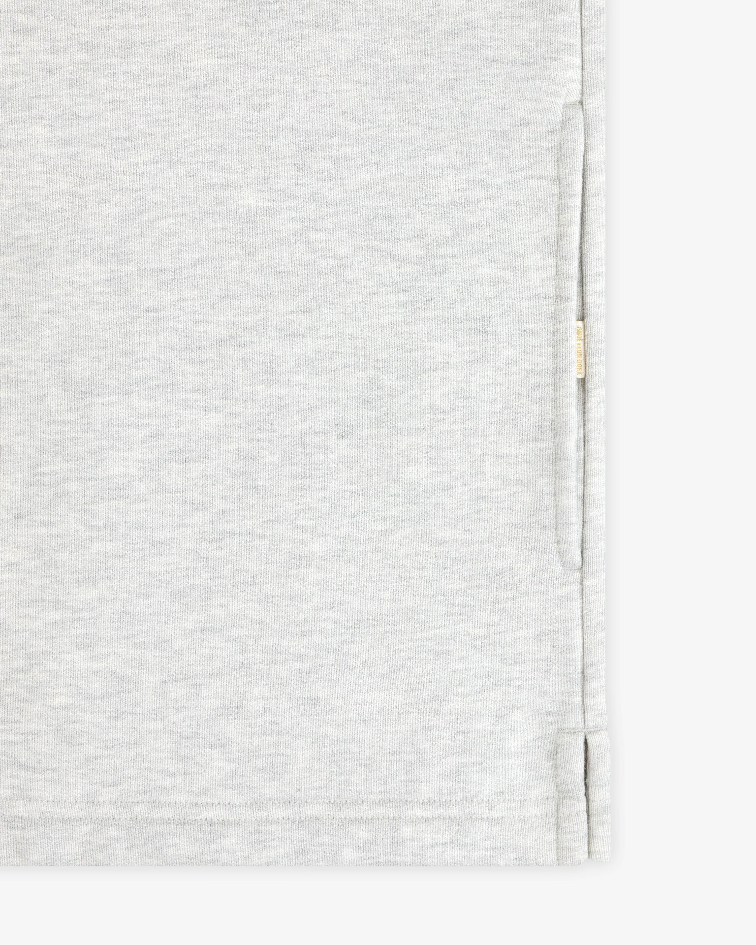 Close-up of the Aimé Souvenir Quarter Zip’s light grey fabric, side seam, hem, and small beige tag on the edge.