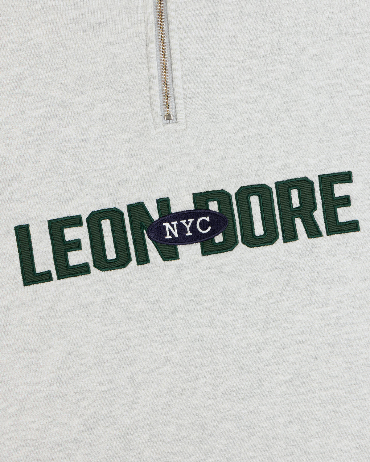 Aimé Souvenir Quarter Zip: cream sweatshirt with green LEON DORE & white NYC on a navy oval in the center.