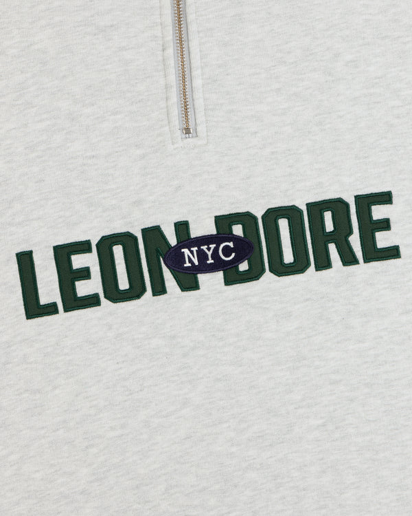 Aimé Souvenir Quarter Zip: cream sweatshirt with green LEON DORE & white NYC on a navy oval in the center.