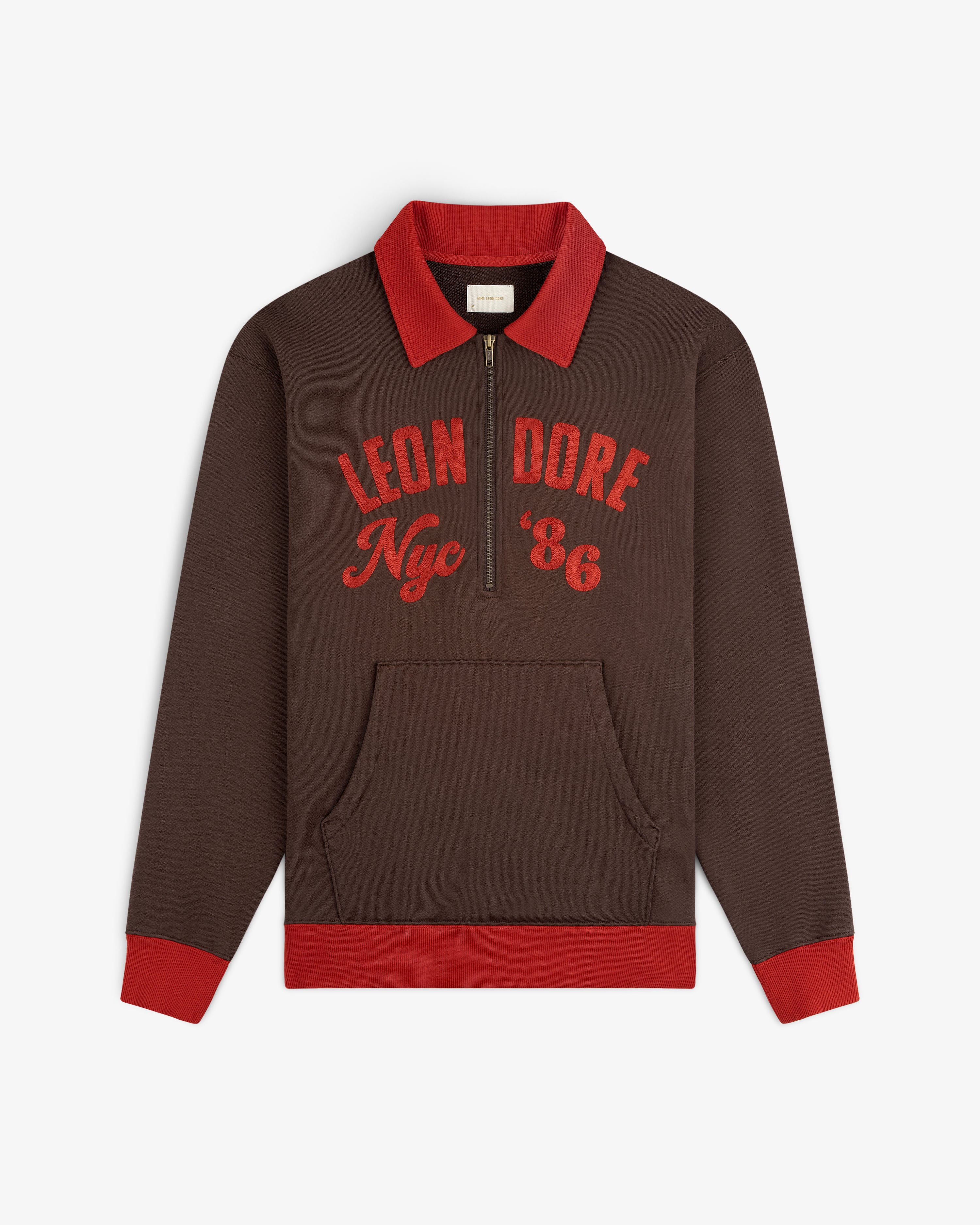 Brown Chainstitch ’86 Half Zip Pullover with a red collar, cuffs, and hem, featuring Leon Dore Nyc 86 on the chest.
