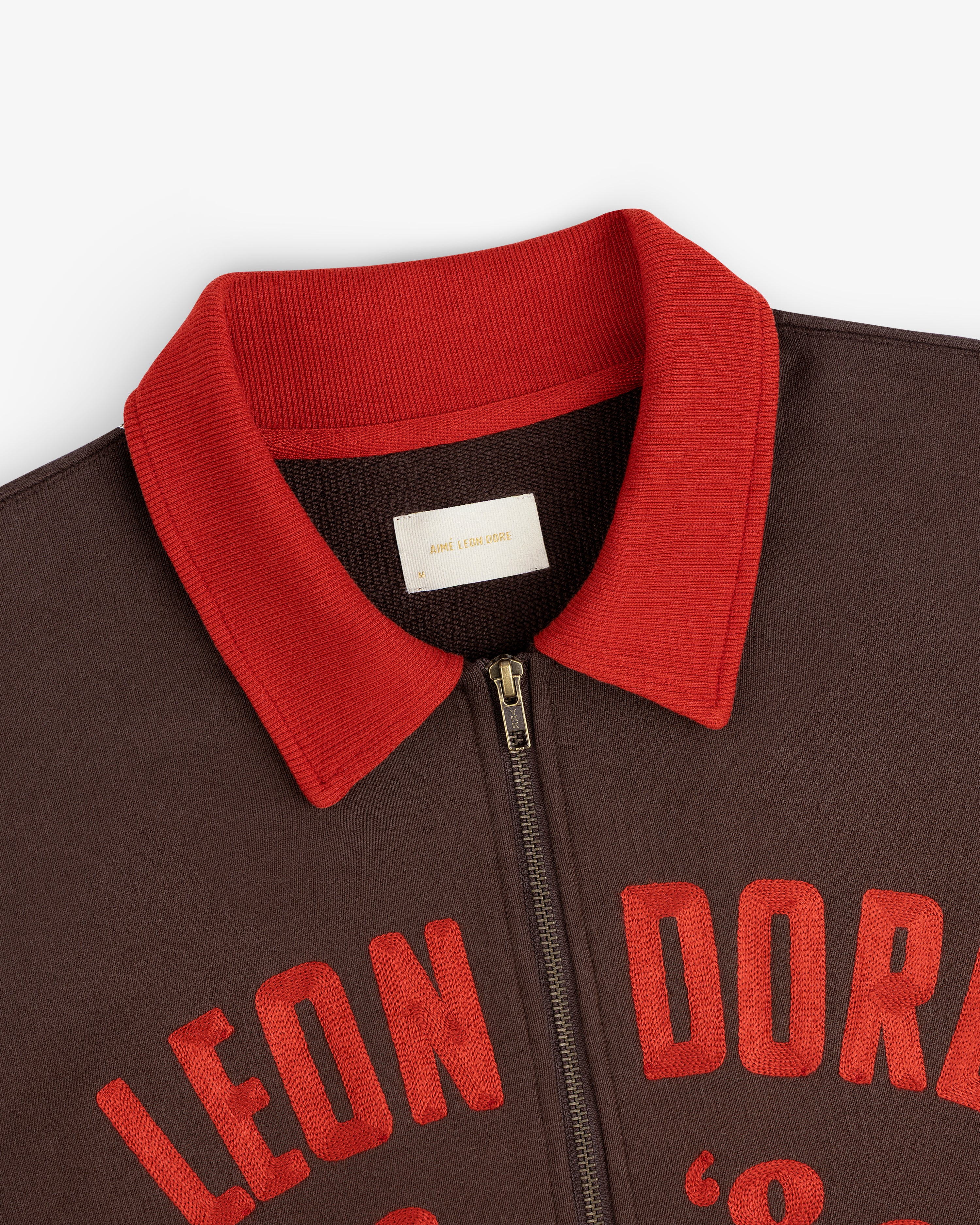 Dark brown Chainstitch ’86 Half Zip Pullover with a red ribbed collar and red embroidered lettering across the chest.