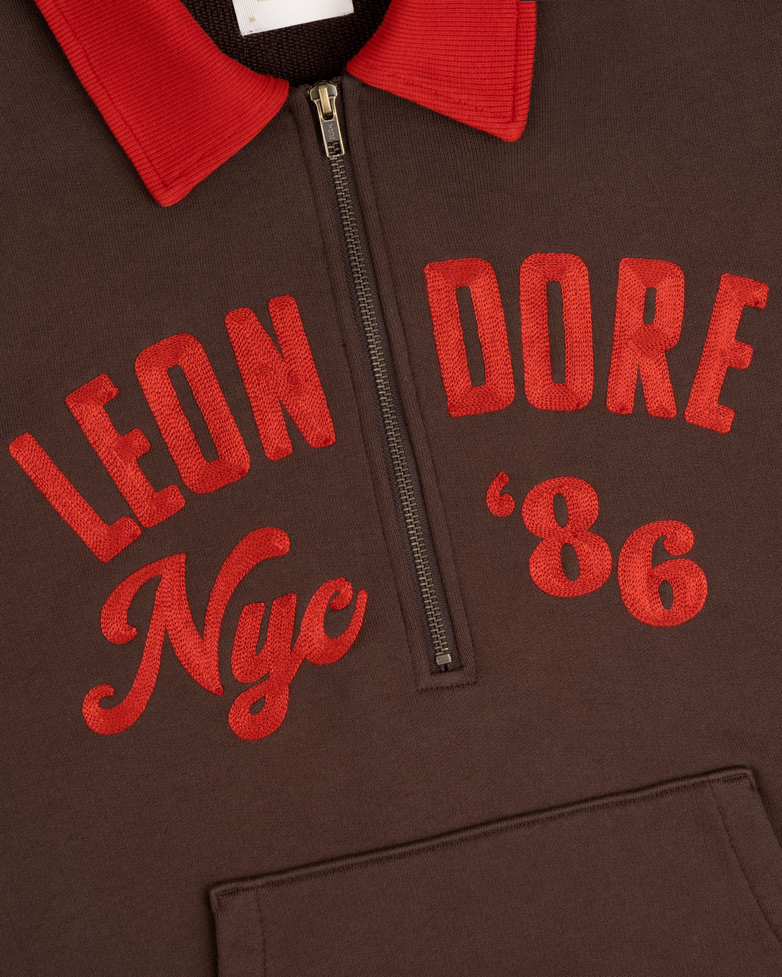 Brown Chainstitch ’86 Half Zip Pullover with a red collar and LEON DORE Nyc 86 embroidered in red on the chest.