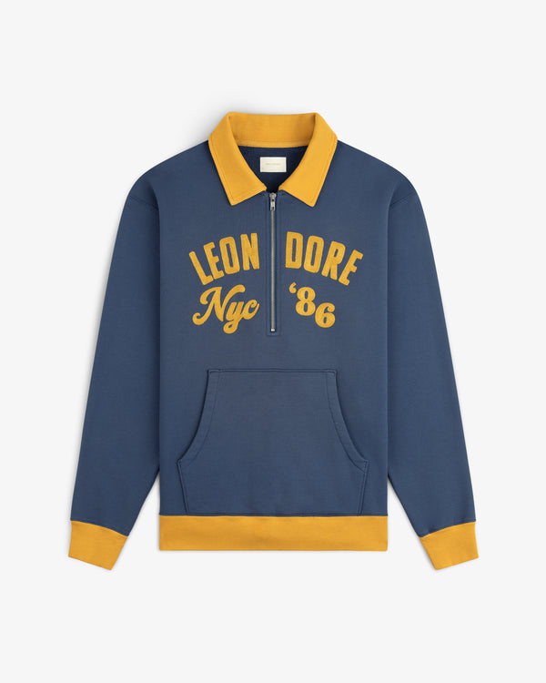 Blue Chainstitch ’86 Half Zip Pullover with a gold collar, cuffs, and hem, featuring LEON DORE Nyc 86 in gold lettering.
