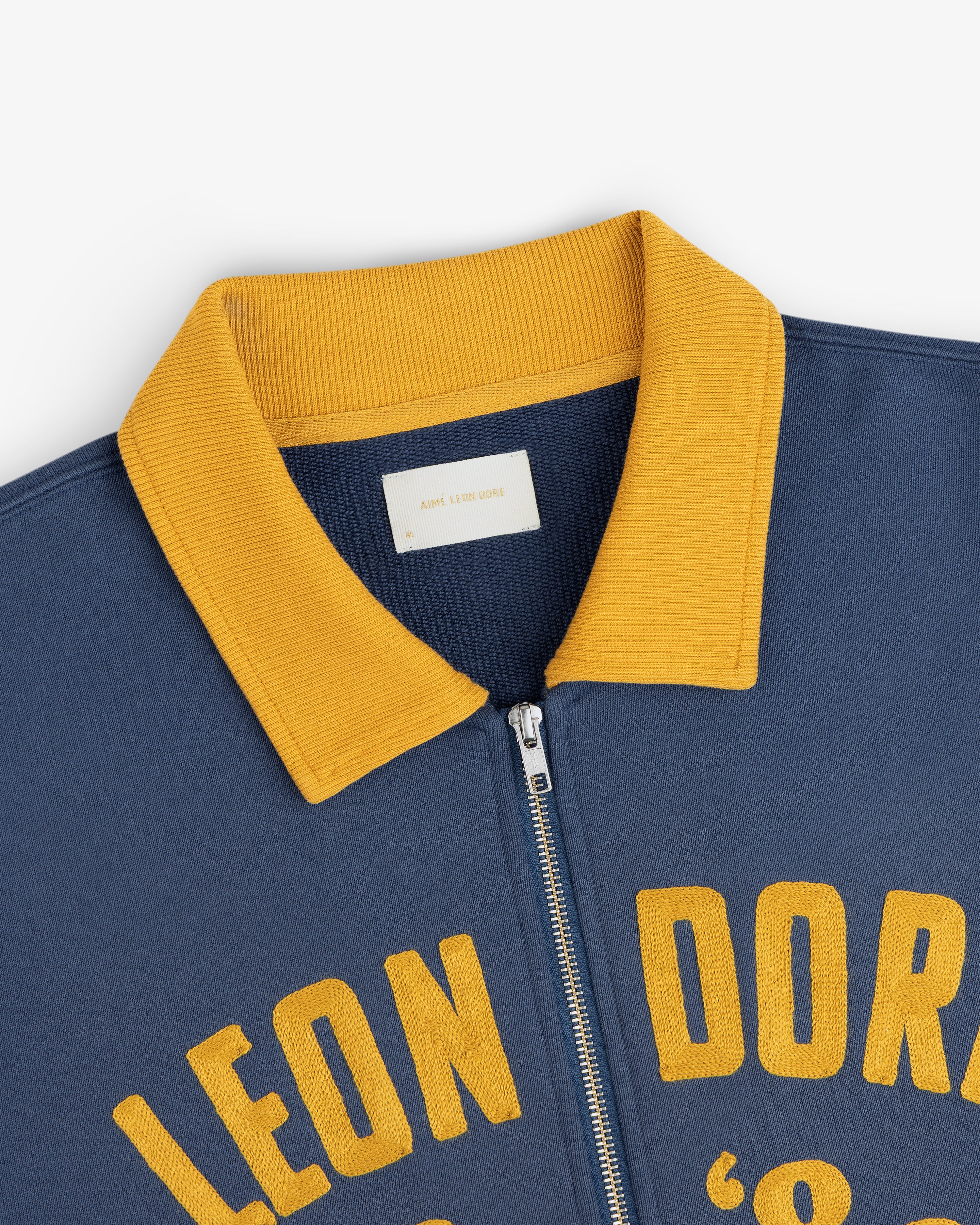 Navy blue Chainstitch ’86 Half Zip Pullover with a yellow ribbed collar and yellow embroidered lettering.
