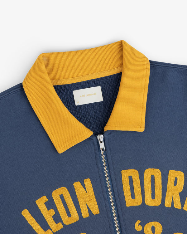 Navy blue Chainstitch ’86 Half Zip Pullover with a yellow ribbed collar and yellow embroidered lettering.