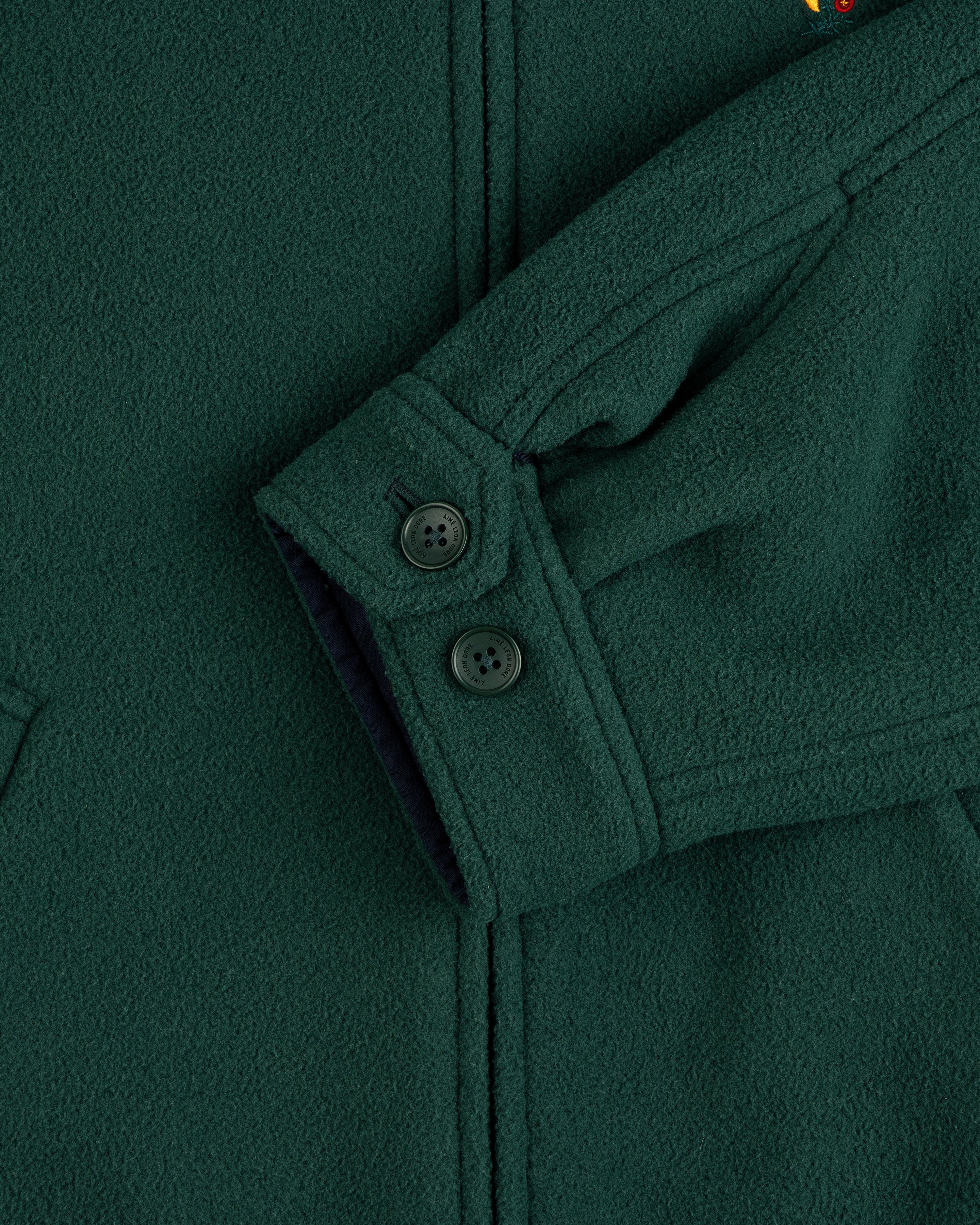 Close-up of a Crest Fleece Casual Jacket sleeve, dark green with 2 black cuff buttons and textured fabric.