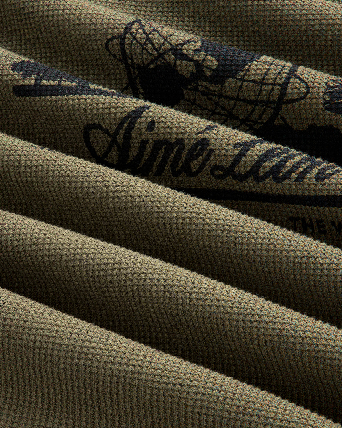 Close-up of ribbed olive green Long-Sleeve Unisphere Waffle Thermal with partial black text and graphic detail.