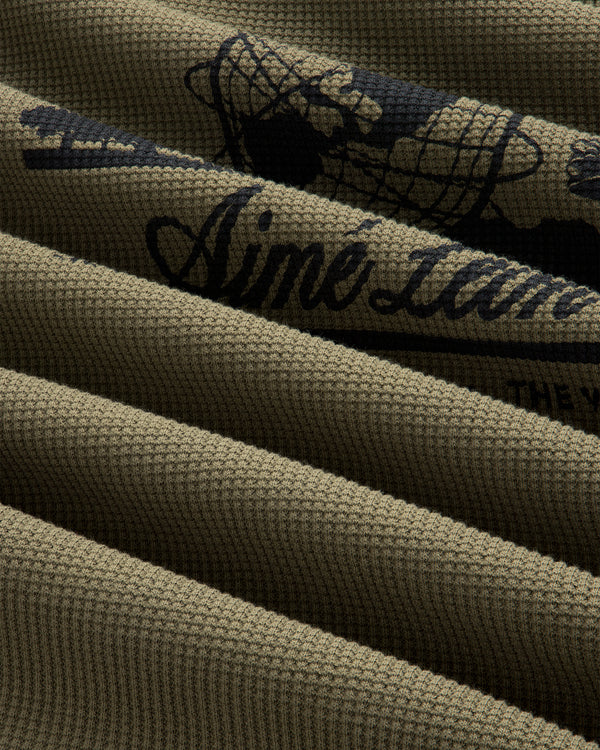 Close-up of ribbed olive green Long-Sleeve Unisphere Waffle Thermal with partial black text and graphic detail.