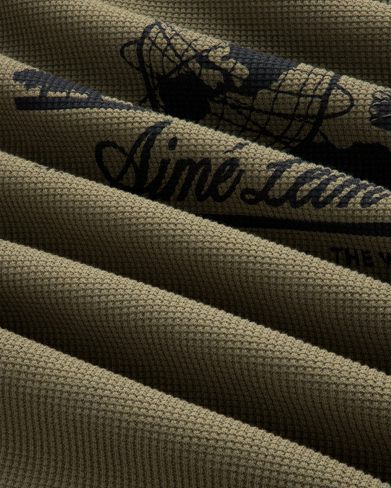 Close-up of ribbed olive green Long-Sleeve Unisphere Waffle Thermal with partial black text and graphic detail.