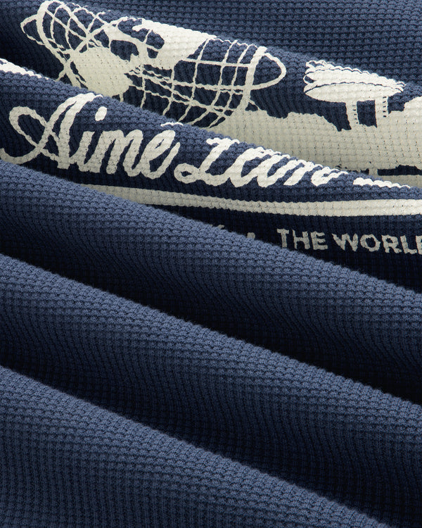 Navy waffle thermal featuring white airplane, globe graphics, and partial “the world” text.