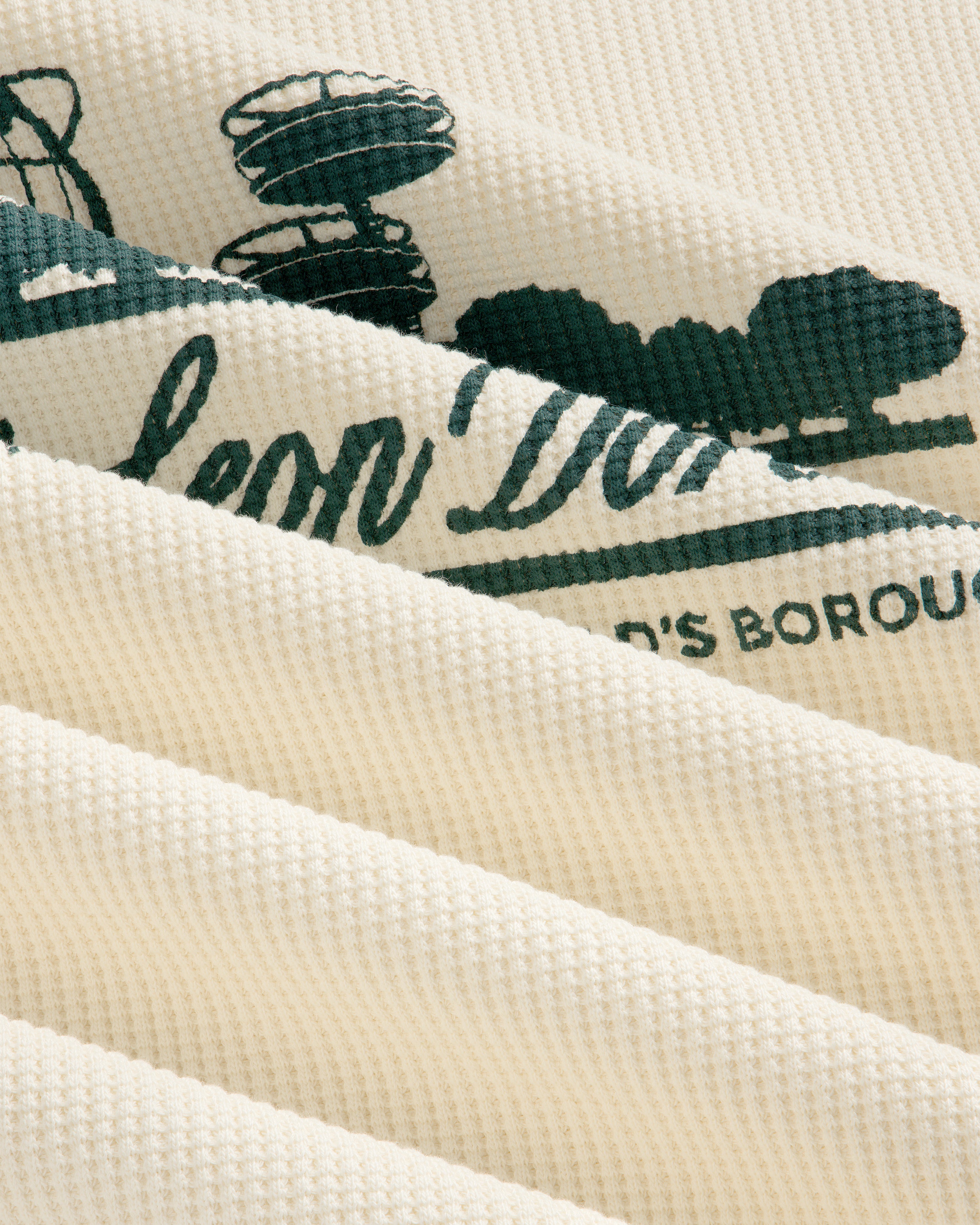 Cream waffle thermal with green Unisphere print, shown close-up with soft folds and ribbed texture.