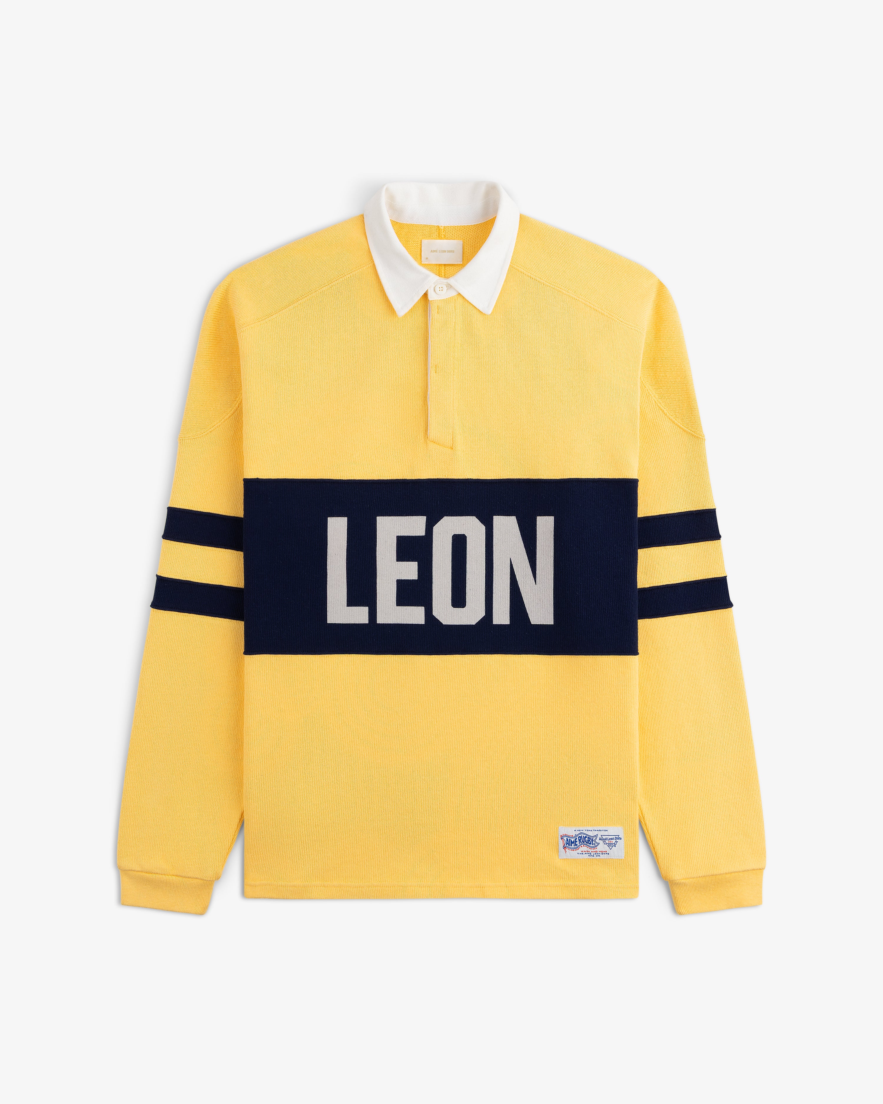 Leon Dore Collegiate Rugby: yellow long-sleeve shirt with navy stripes, bold LEON front, white collar, button placket.