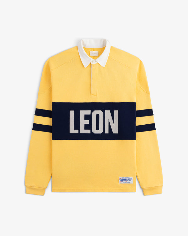 Leon Dore Collegiate Rugby: yellow long-sleeve shirt with navy stripes, bold LEON front, white collar, button placket.