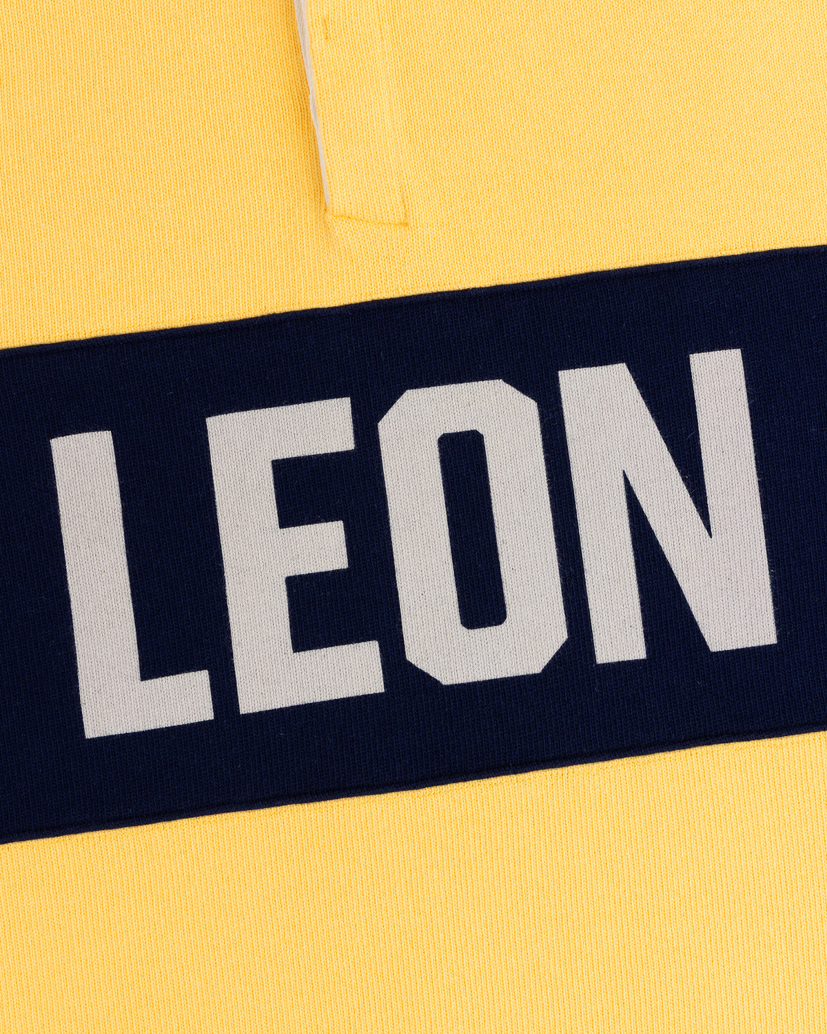 Yellow Leon Dore Collegiate Rugby with a navy stripe and bold, white uppercase LEON text.