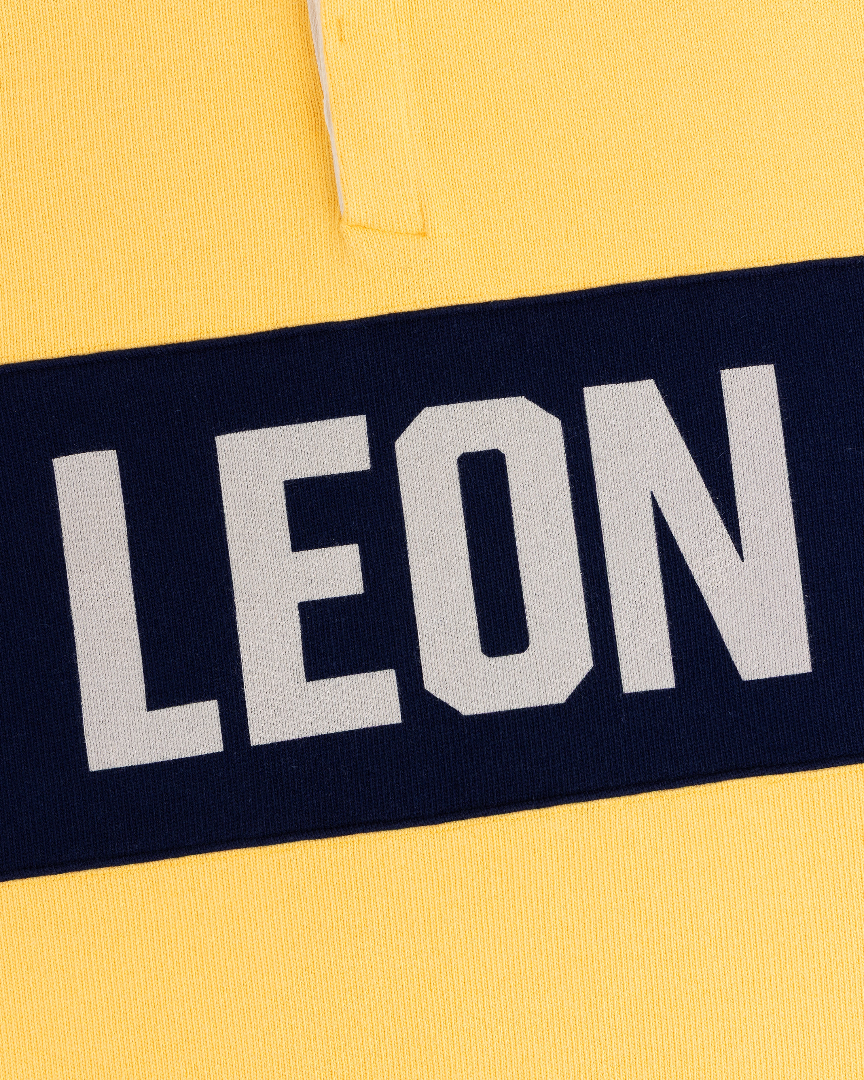 Yellow Leon Dore Collegiate Rugby with a navy stripe and bold, white uppercase LEON text.
