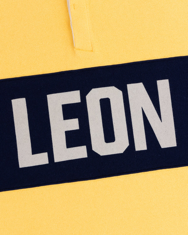 Yellow Leon Dore Collegiate Rugby with a navy stripe and bold, white uppercase LEON text.