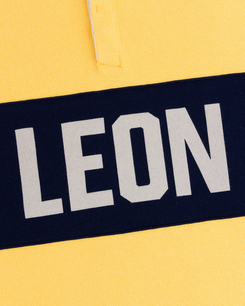 Yellow Leon Dore Collegiate Rugby with a navy stripe and bold, white uppercase LEON text.