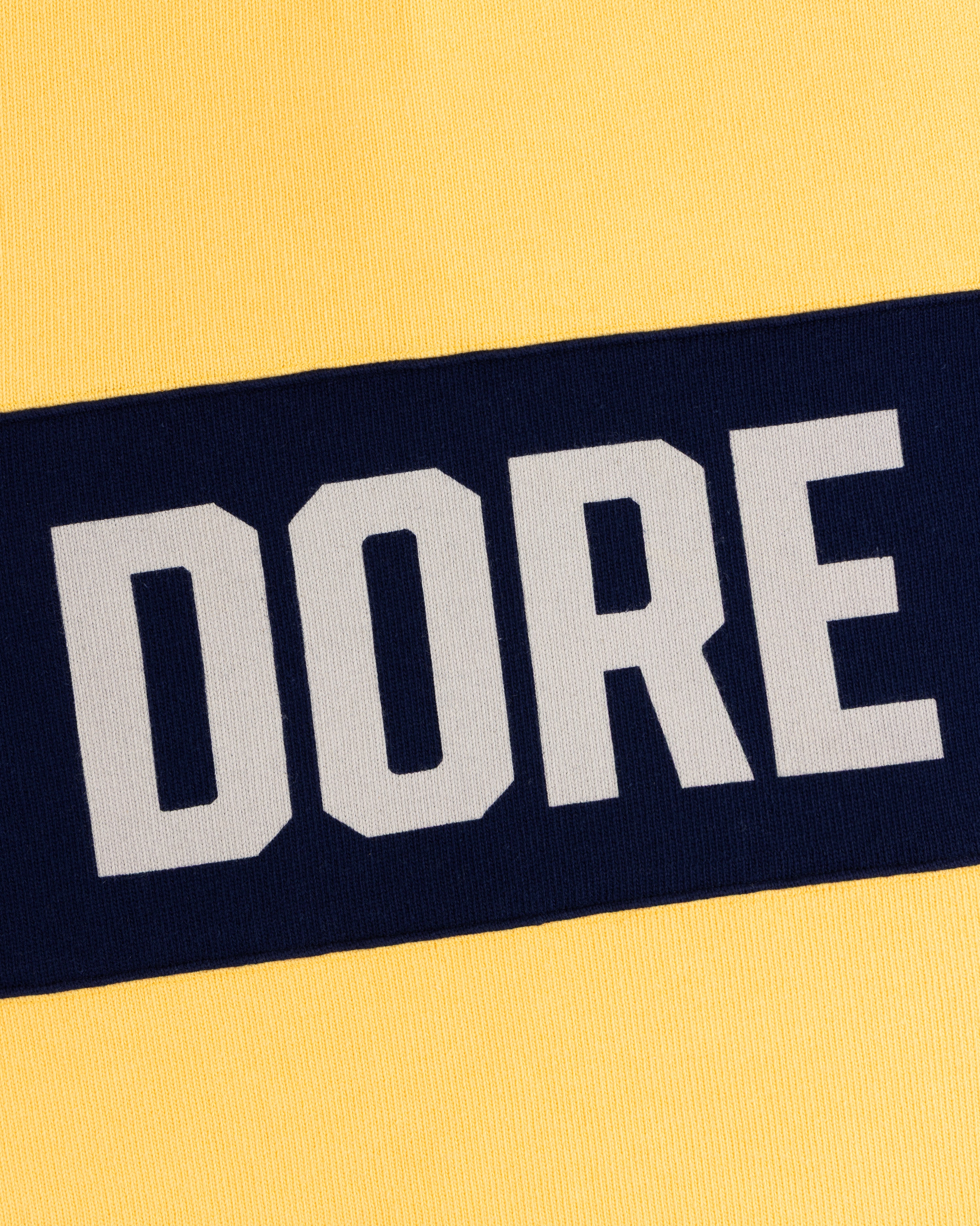 Yellow fabric with a bold navy stripe and “DORE” on the Leon Dore Collegiate Rugby.