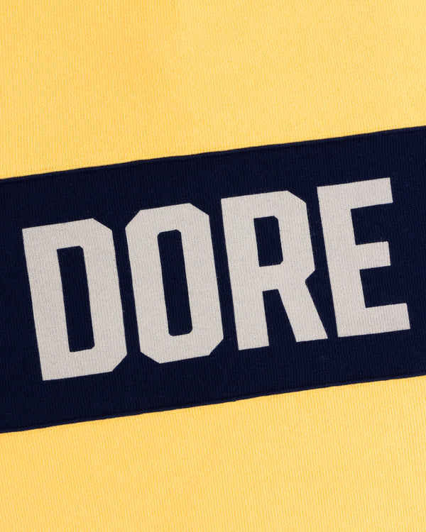Yellow fabric with a bold navy stripe and “DORE” on the Leon Dore Collegiate Rugby.