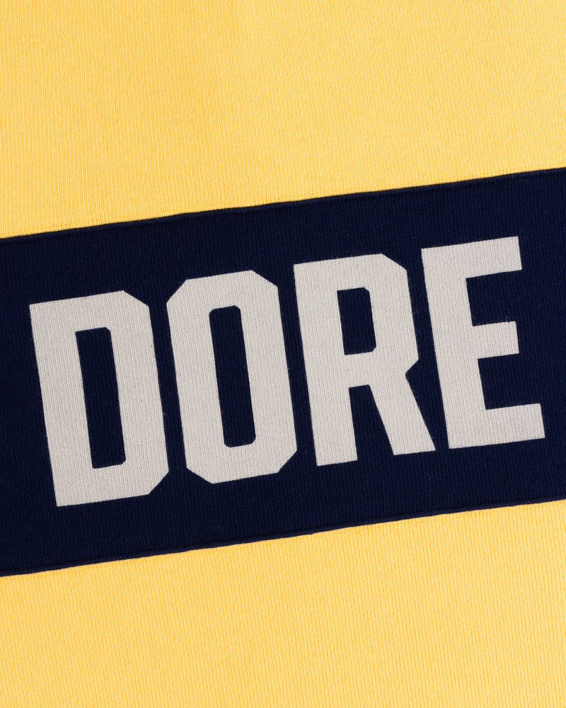 Yellow fabric with a bold navy stripe and “DORE” on the Leon Dore Collegiate Rugby.