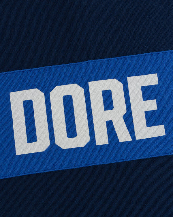 The Leon Dore Collegiate Rugby wordmark in white on blue, set against a dark blue background.