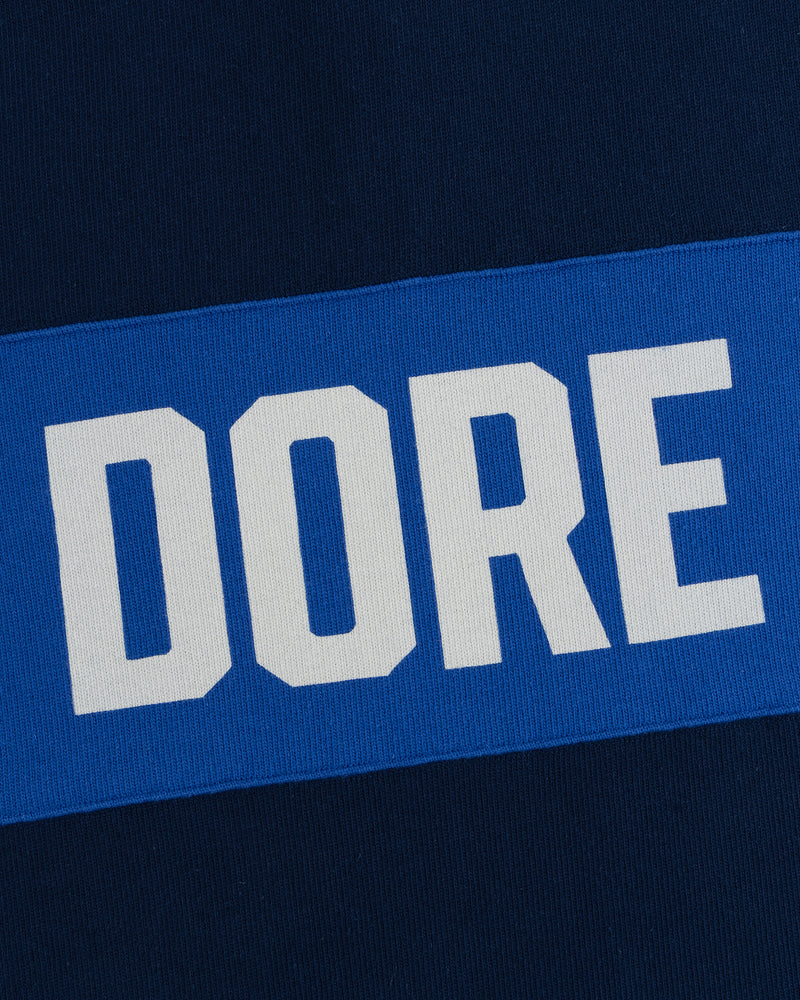 The Leon Dore Collegiate Rugby wordmark in white on blue, set against a dark blue background.