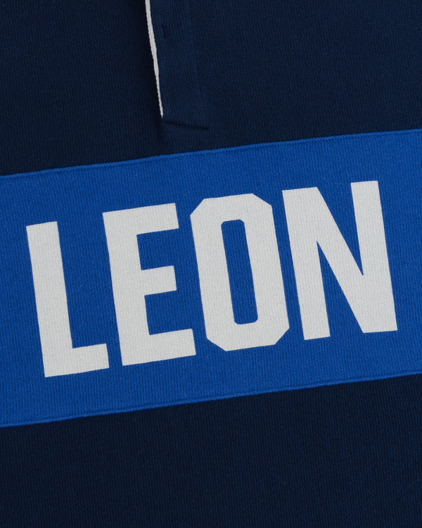 LEON in white caps on a blue stripe, set on a dark blue Leon Dore Collegiate Rugby background.