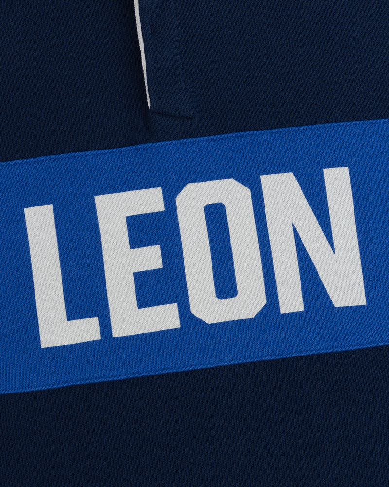 LEON in white caps on a blue stripe, set on a dark blue Leon Dore Collegiate Rugby background.