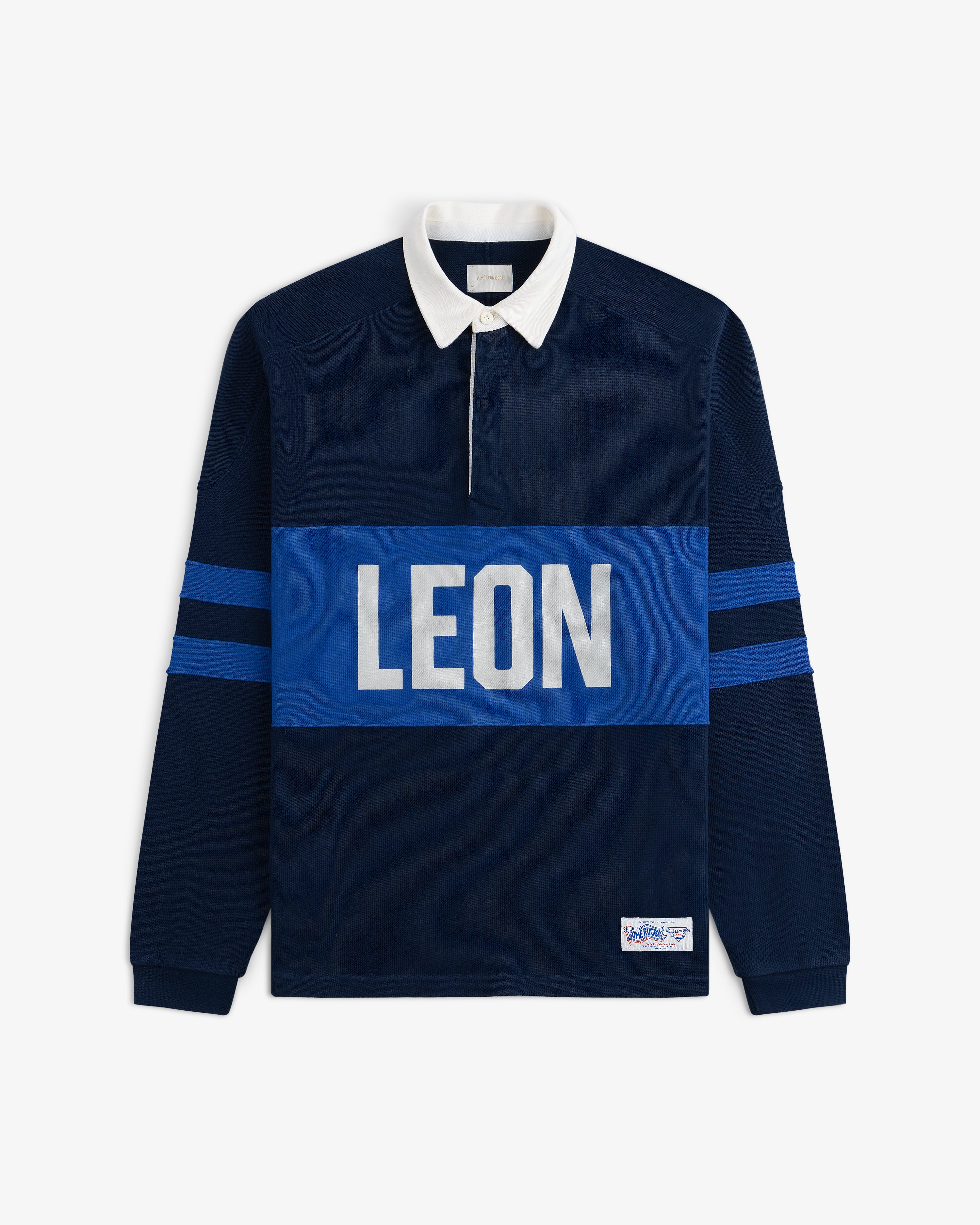 Leon Dore Collegiate Rugby—navy shirt with white collar, blue sleeve stripes, and bold LEON chest print.