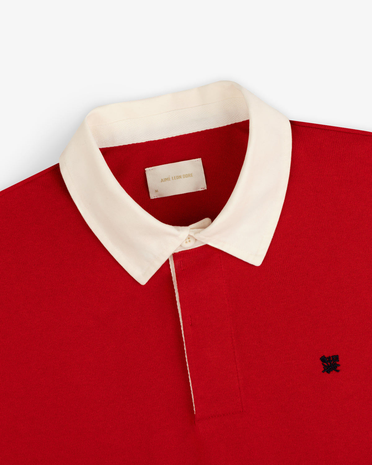 Crest Rugby red polo with white collar and dark chest logo, top-down view on a white background.