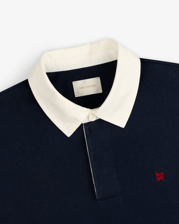 Crest Rugby: Navy shirt with white collar, white buttons, and red embroidered left-chest logo.