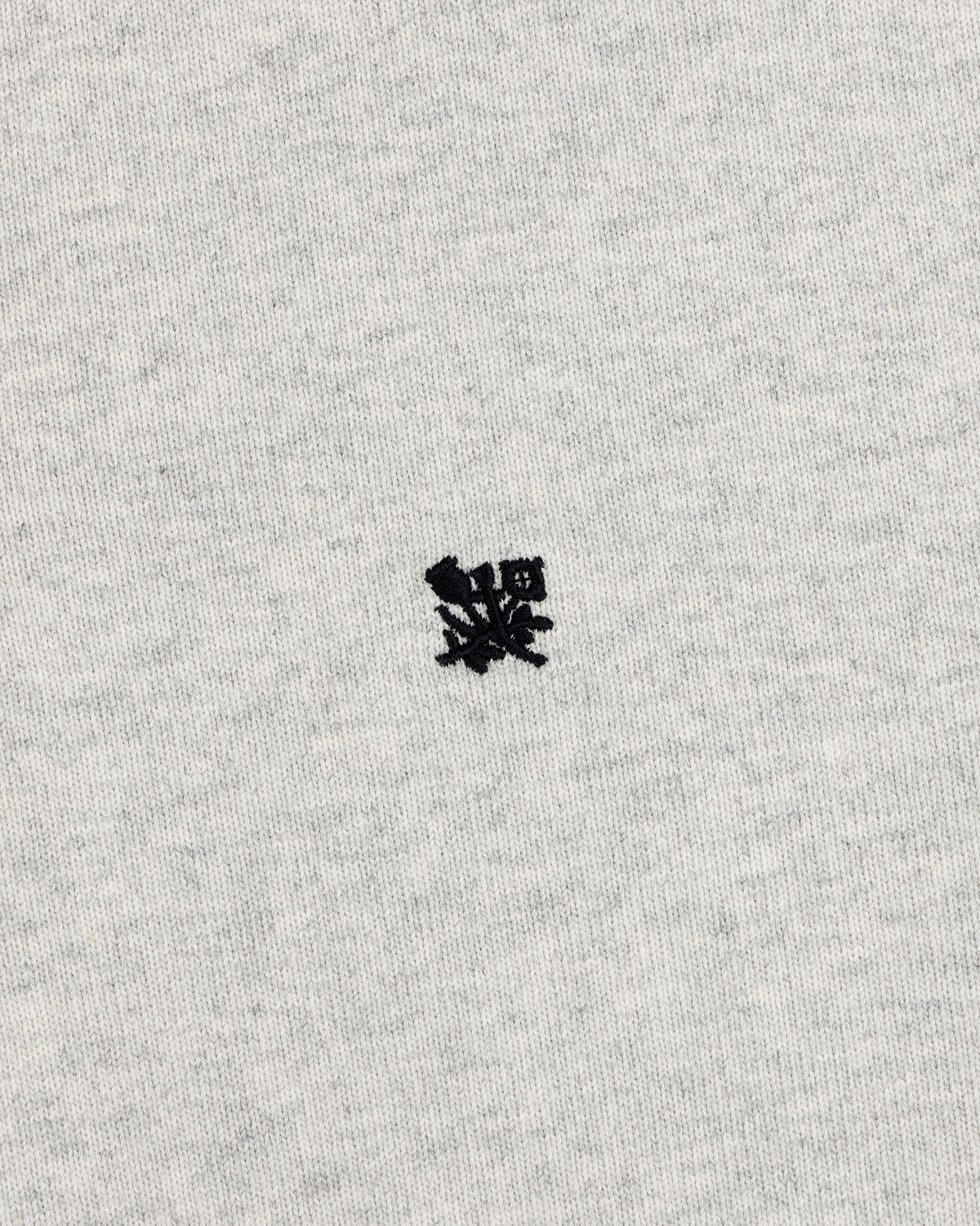 Small black embroidered Crest Rugby logo on light gray fabric, centered with minimal texture.