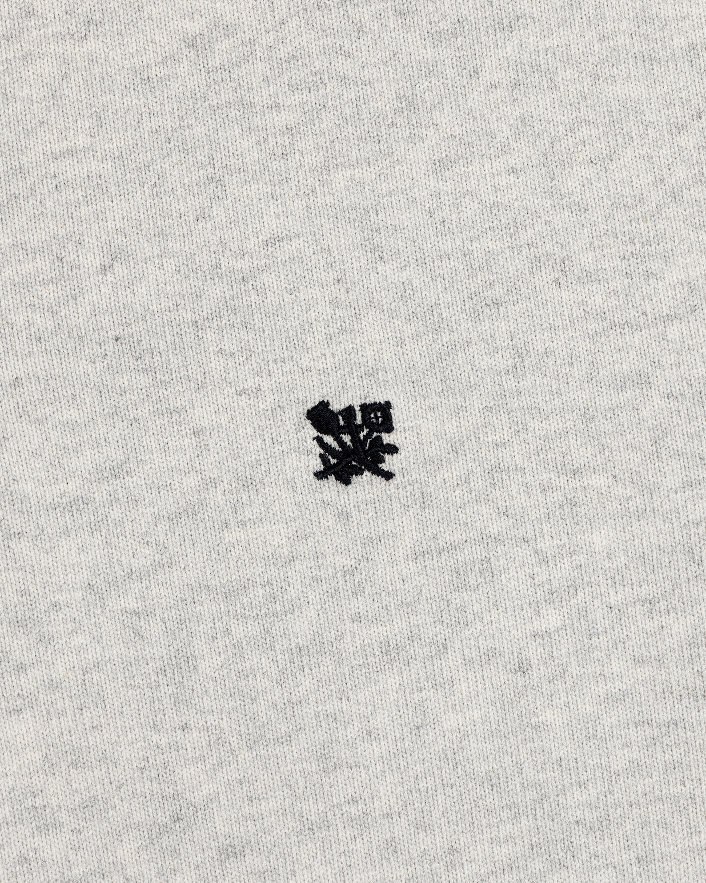 Small black embroidered Crest Rugby logo on light gray fabric, centered with minimal texture.