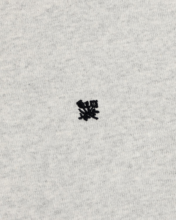 Small black embroidered Crest Rugby logo on light gray fabric, centered with minimal texture.