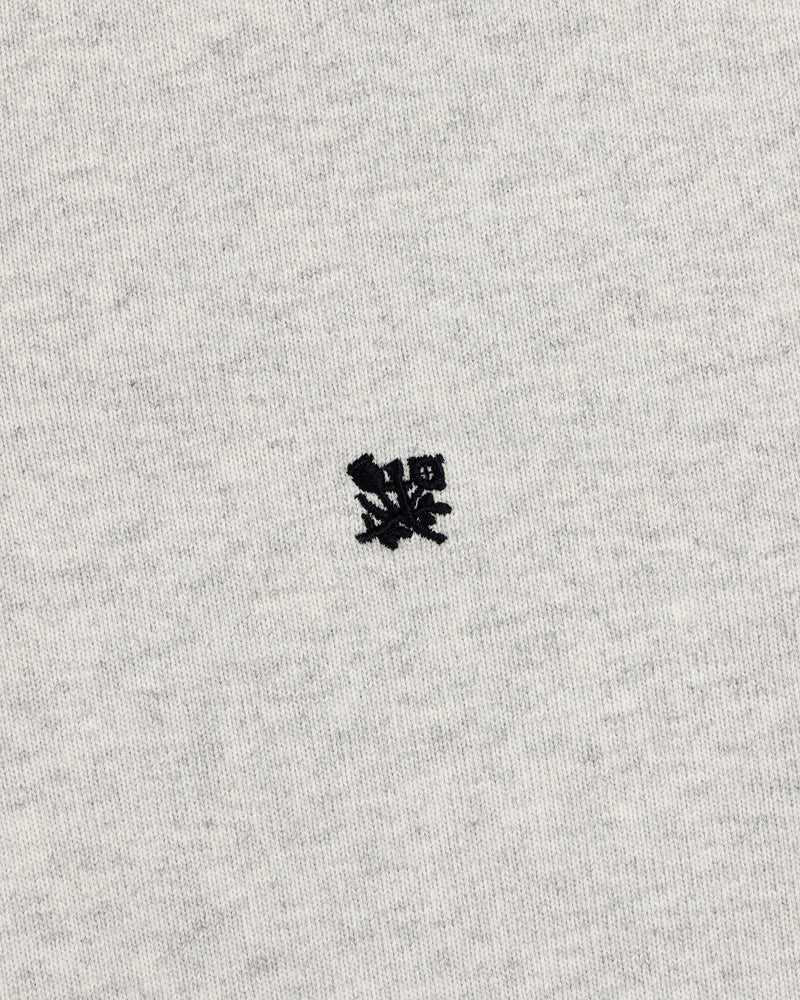 Small black embroidered Crest Rugby logo on light gray fabric, centered with minimal texture.