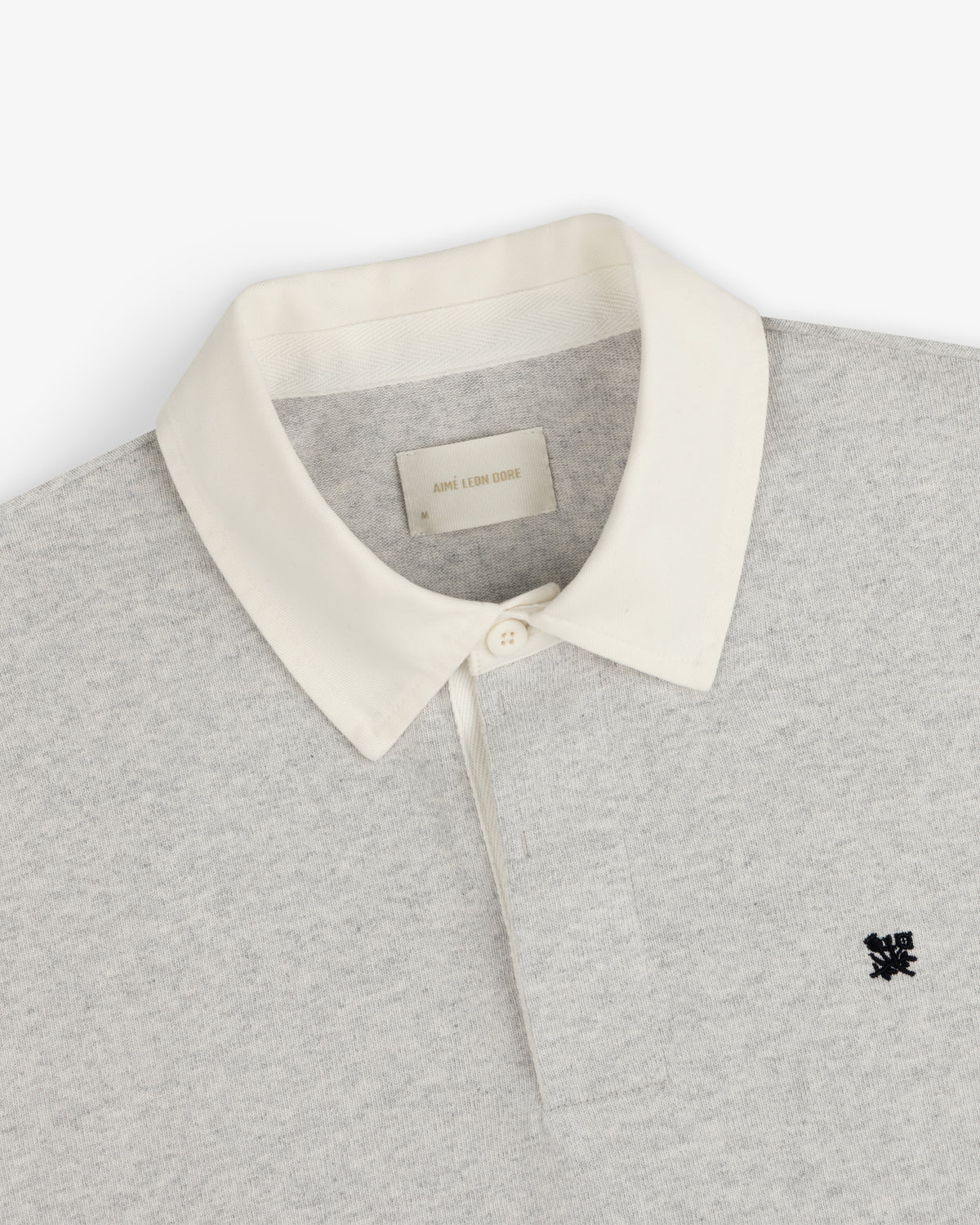 Crest Rugby: Light gray rugby shirt with white collar, single button, and small black chest logo.