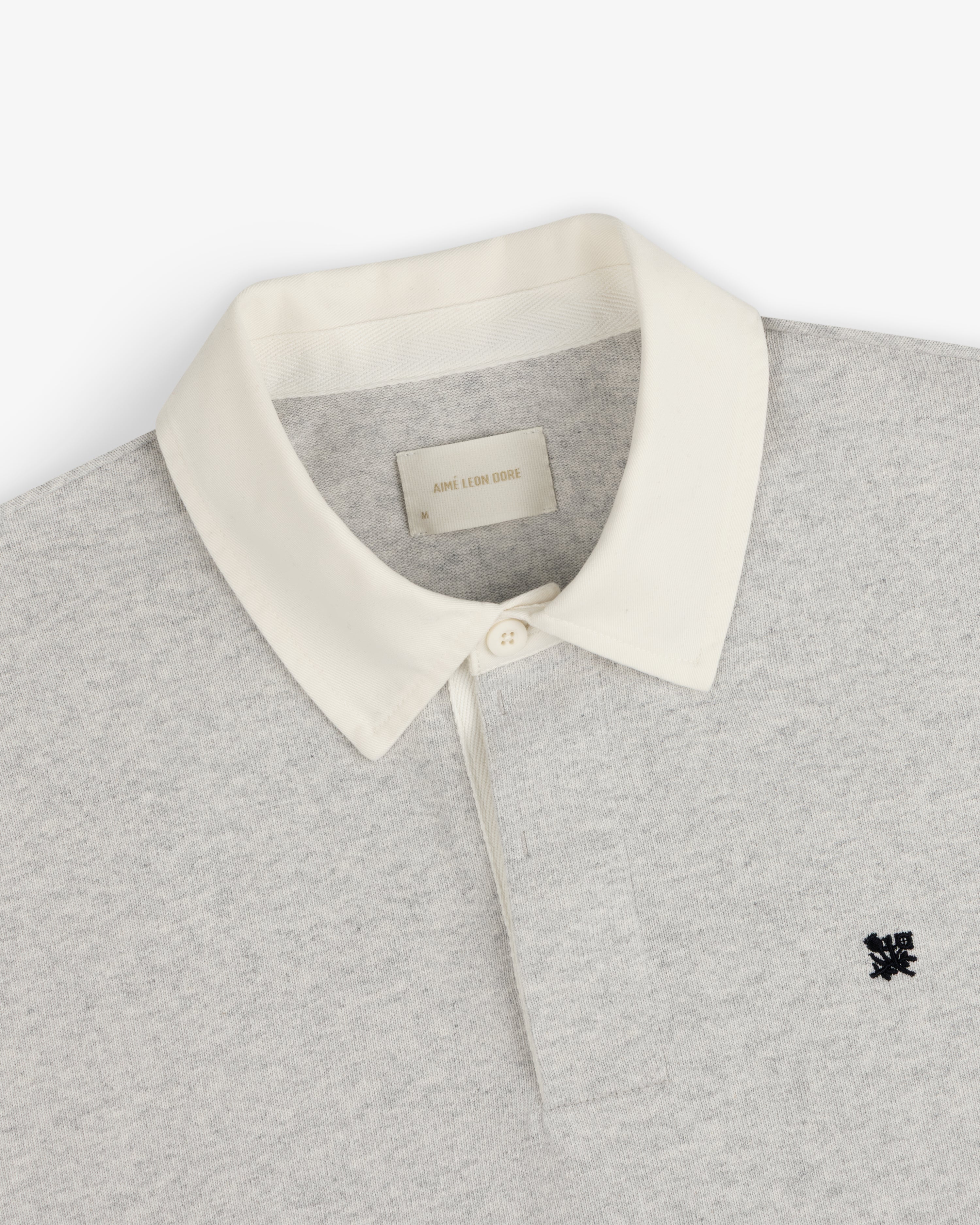 Crest Rugby: Light gray rugby shirt with white collar, single button, and small black chest logo.