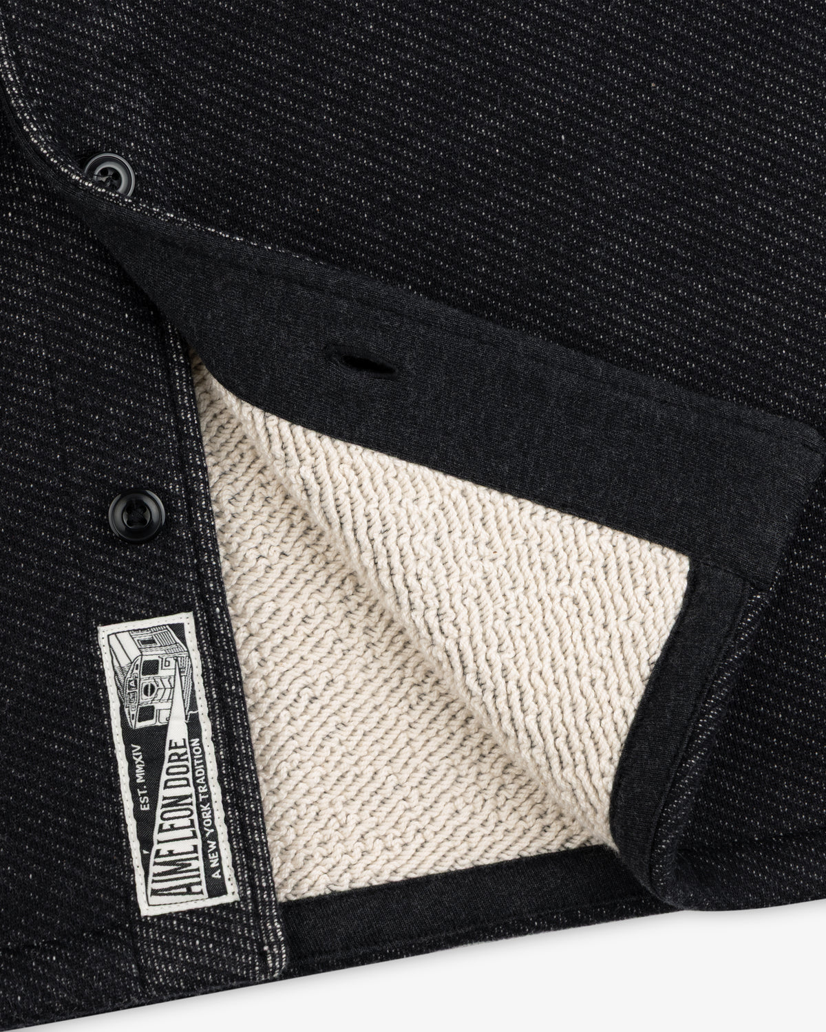 Close-up of a black Terry Lounge shirt with a textured, beige terry cloth interior and a branded label at the hem.