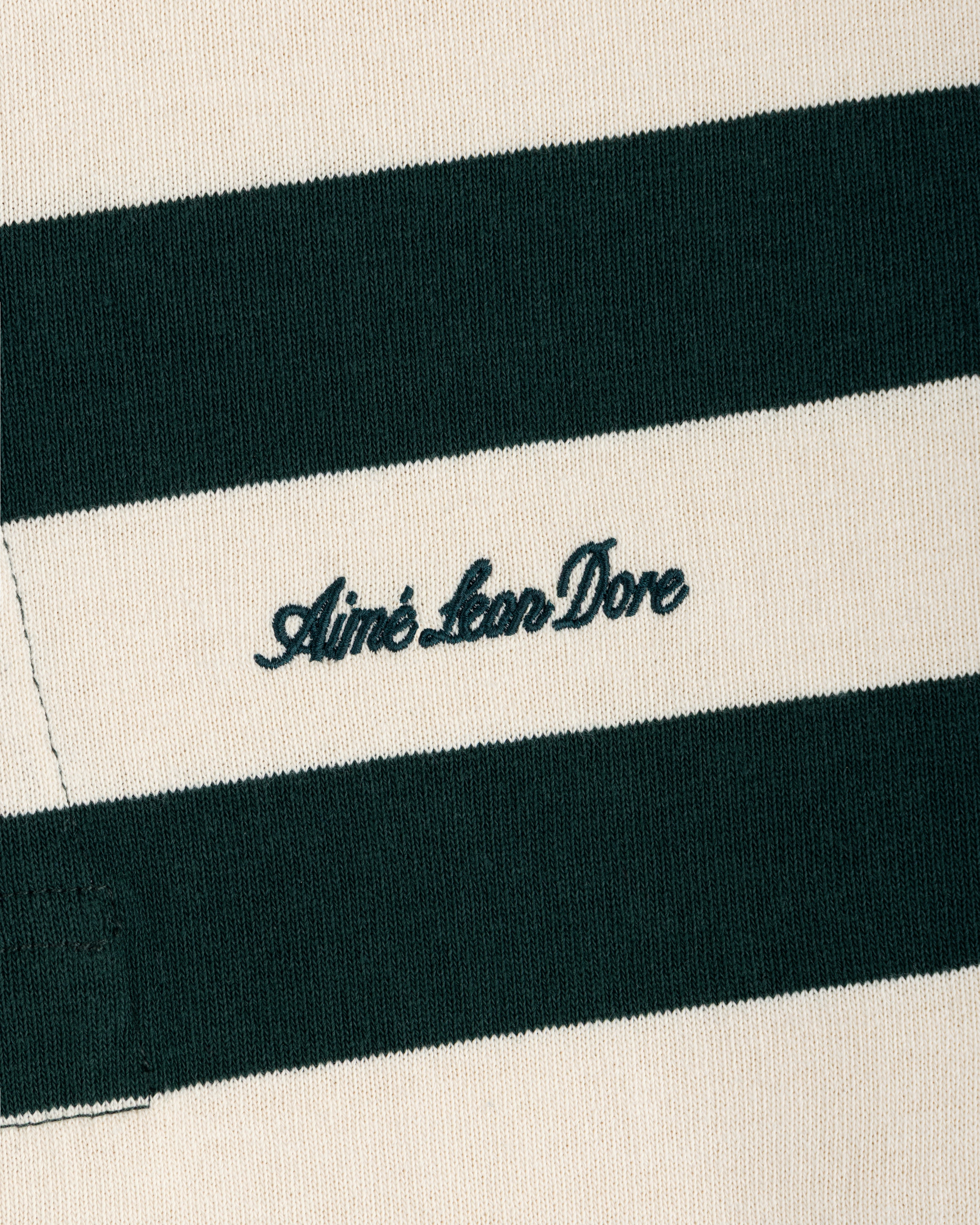 Close-up of a Striped Script Rugby shirt in dark green and off-white with the brand name embroidered in script.