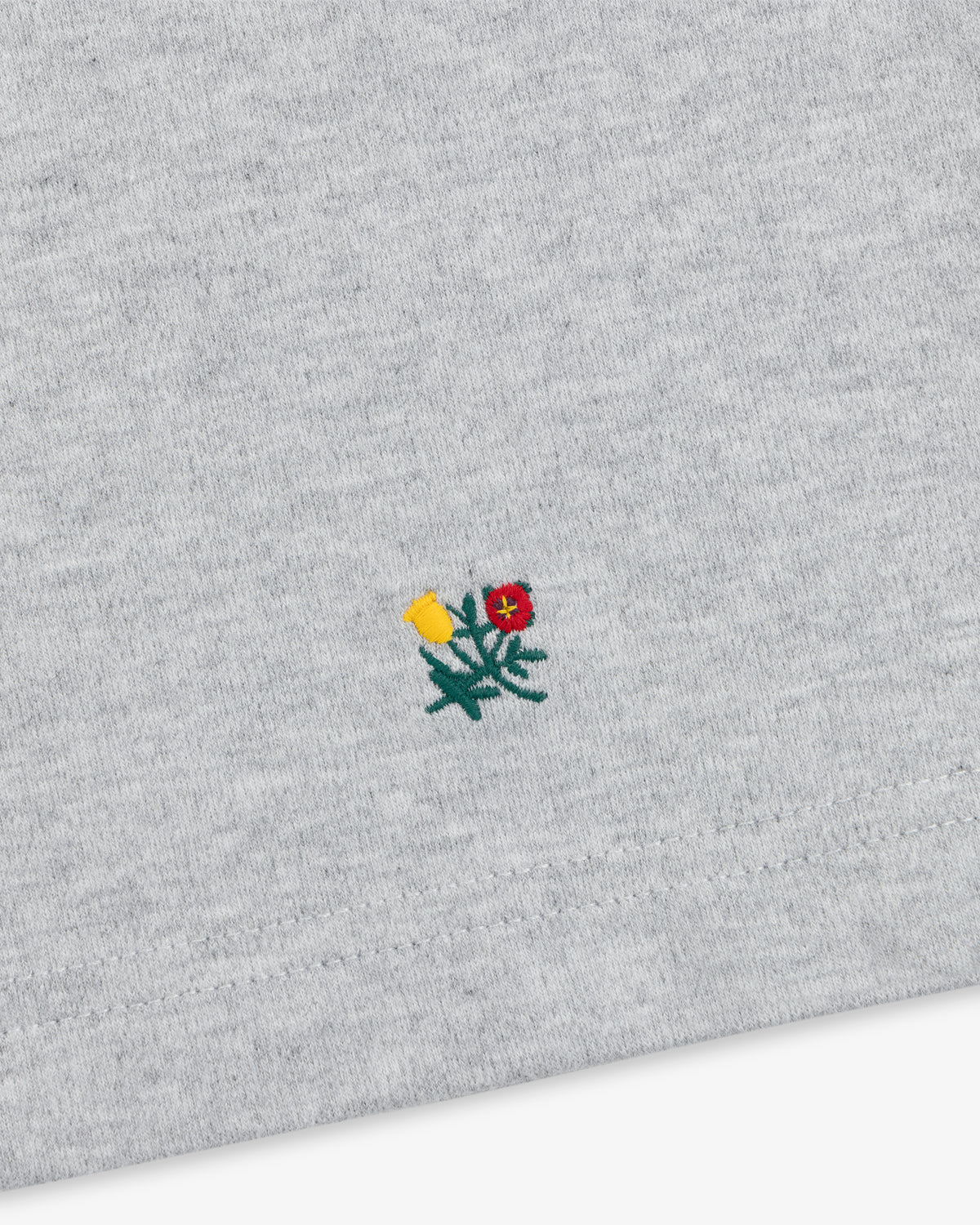 Heavyweight Crest Mockneck Tee in grey heathered fabric with a small embroidered yellow and red flower emblem.