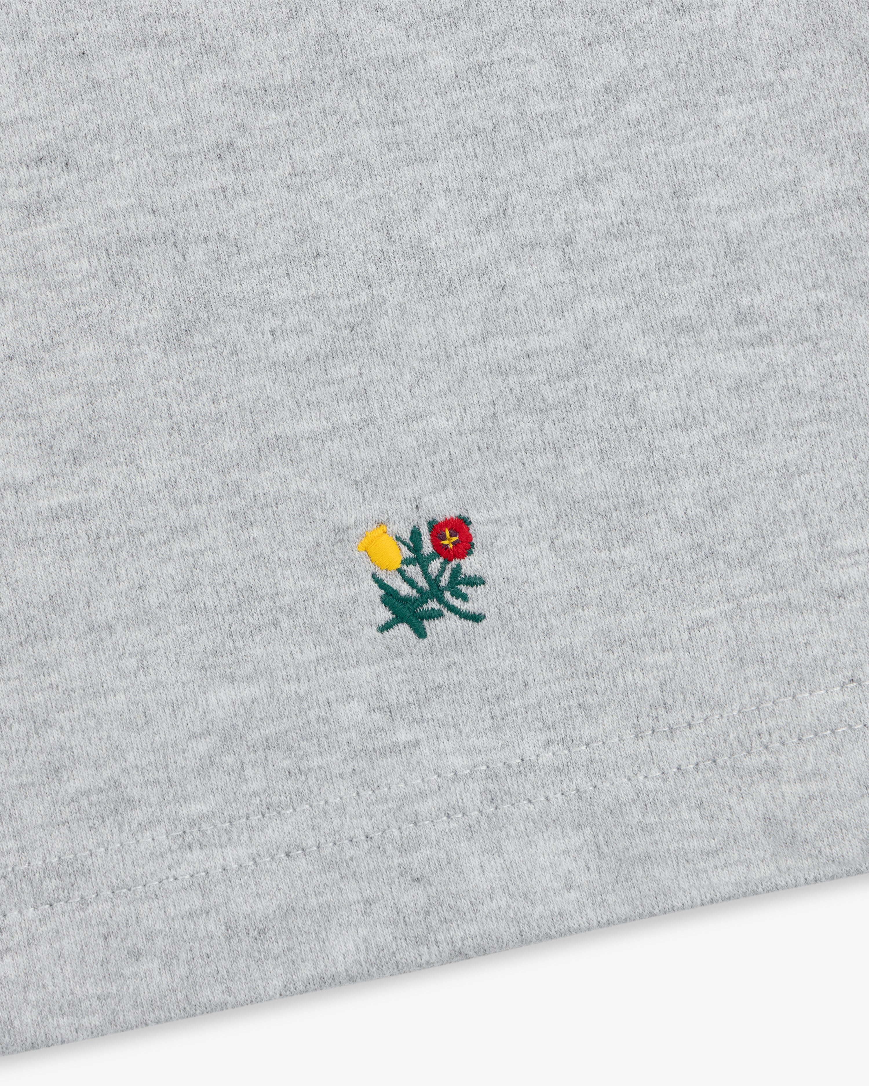 Heavyweight Crest Mockneck Tee in grey heathered fabric with a small embroidered yellow and red flower emblem.
