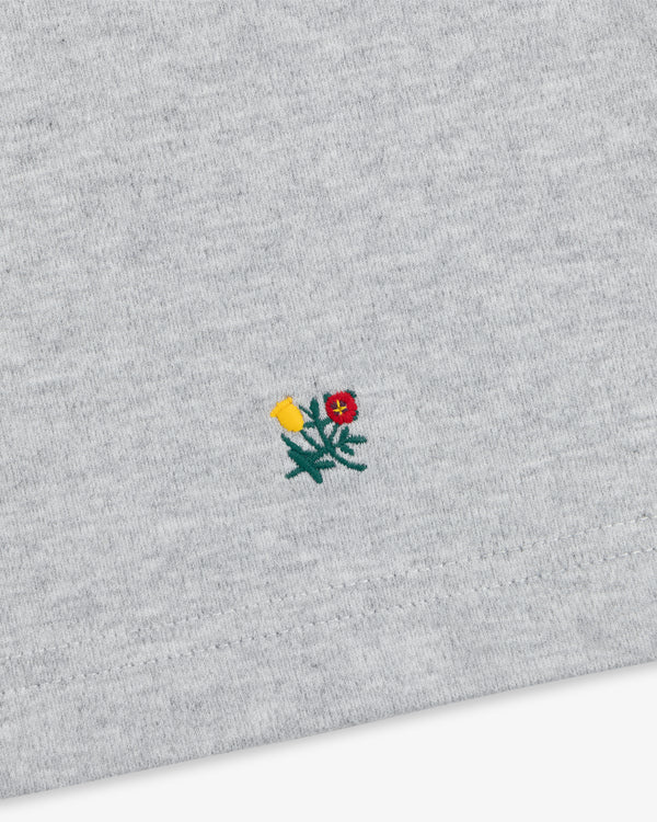 Heavyweight Crest Mockneck Tee in grey heathered fabric with a small embroidered yellow and red flower emblem.