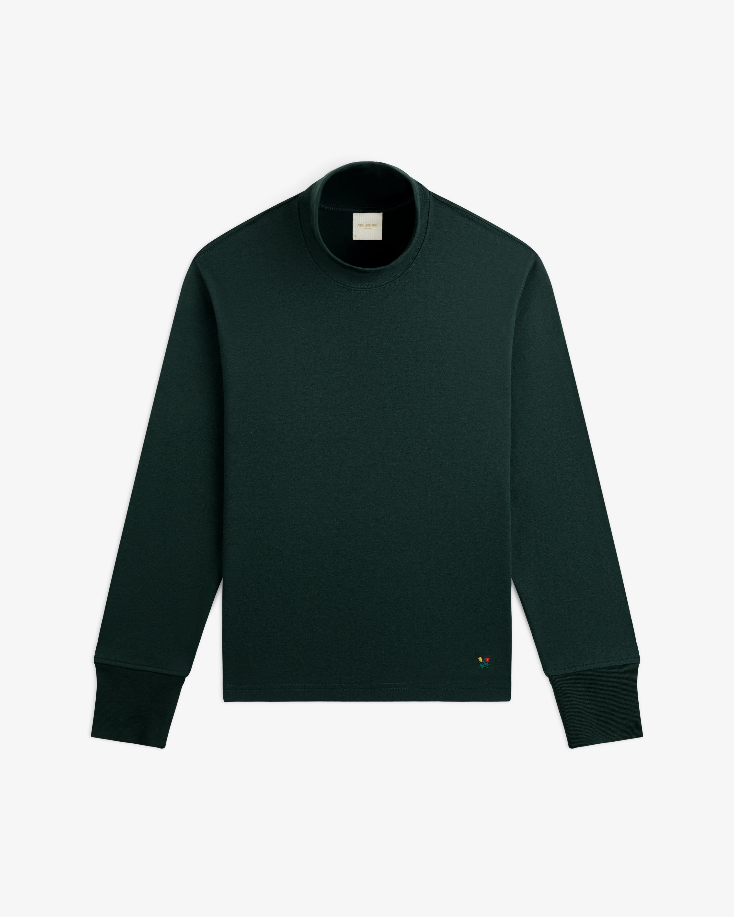 Heavyweight Crest Mockneck Tee in dark green with ribbed cuffs and a small flower icon near the hem.