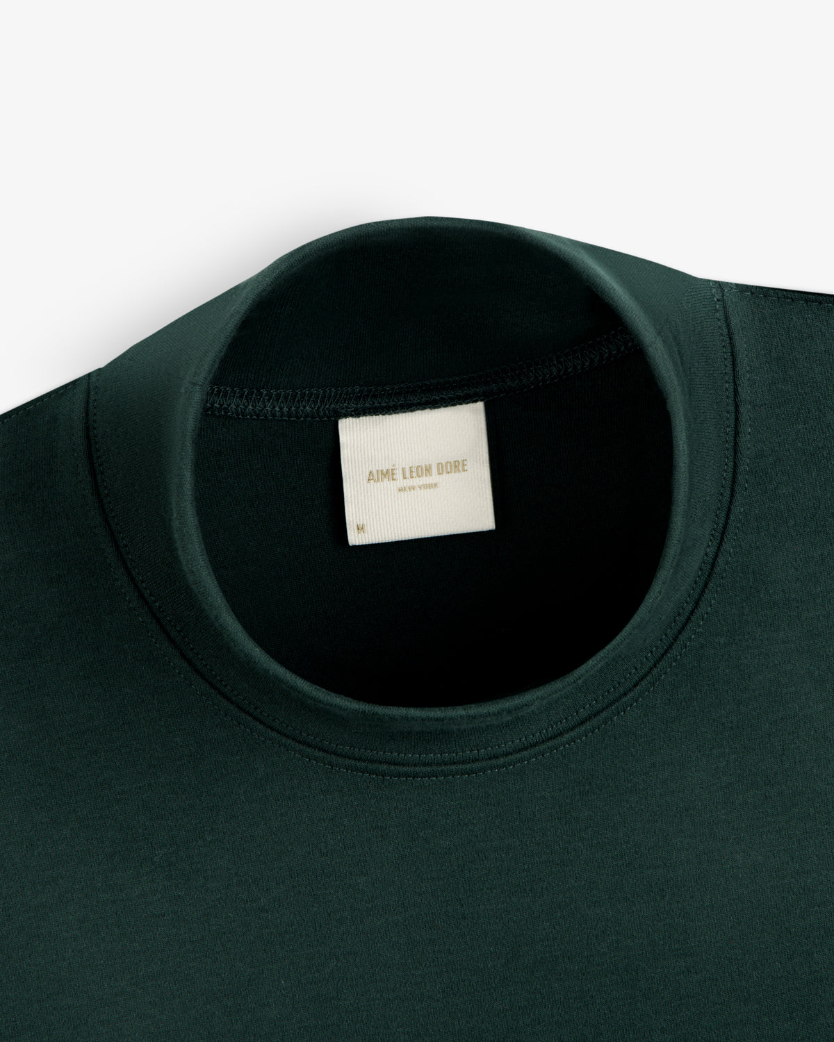 Dark green Heavyweight Crest Mockneck Tee with a neck label reading Aimé Leon Dore New York.