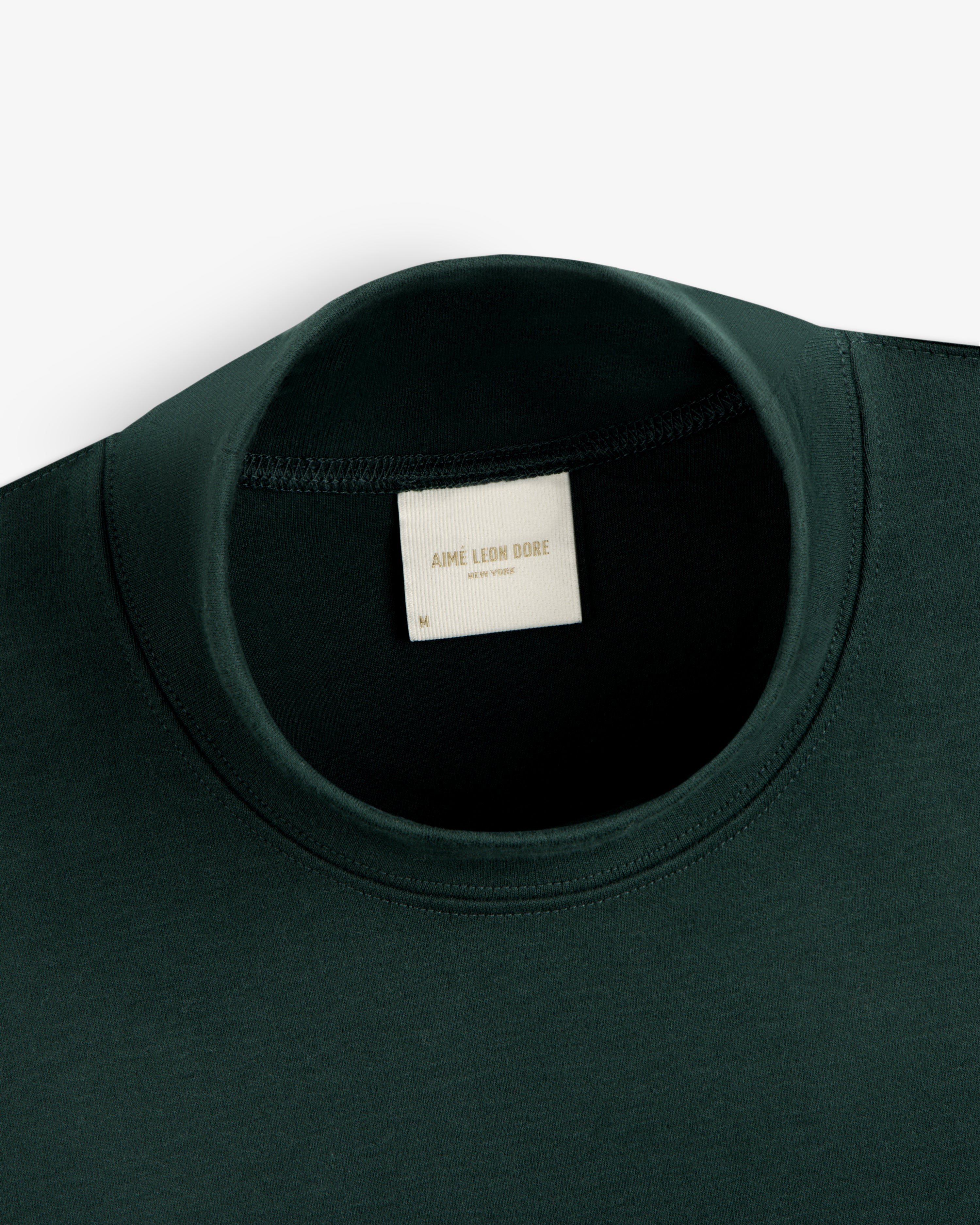 Dark green Heavyweight Crest Mockneck Tee with a neck label reading Aimé Leon Dore New York.