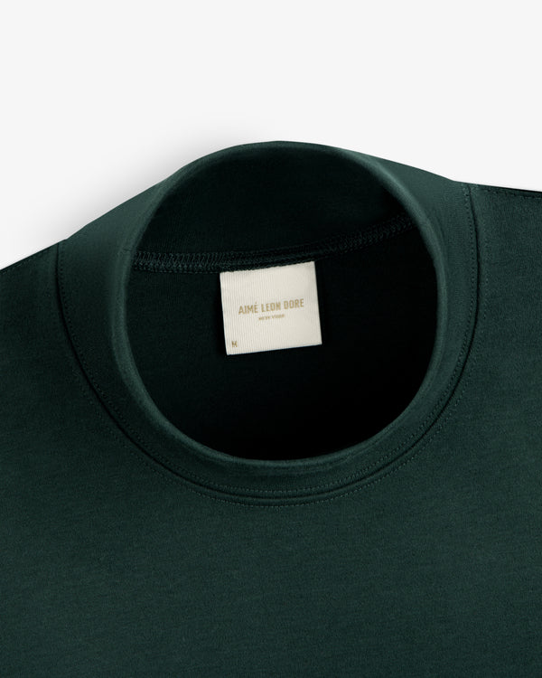 Dark green Heavyweight Crest Mockneck Tee with a neck label reading Aimé Leon Dore New York.