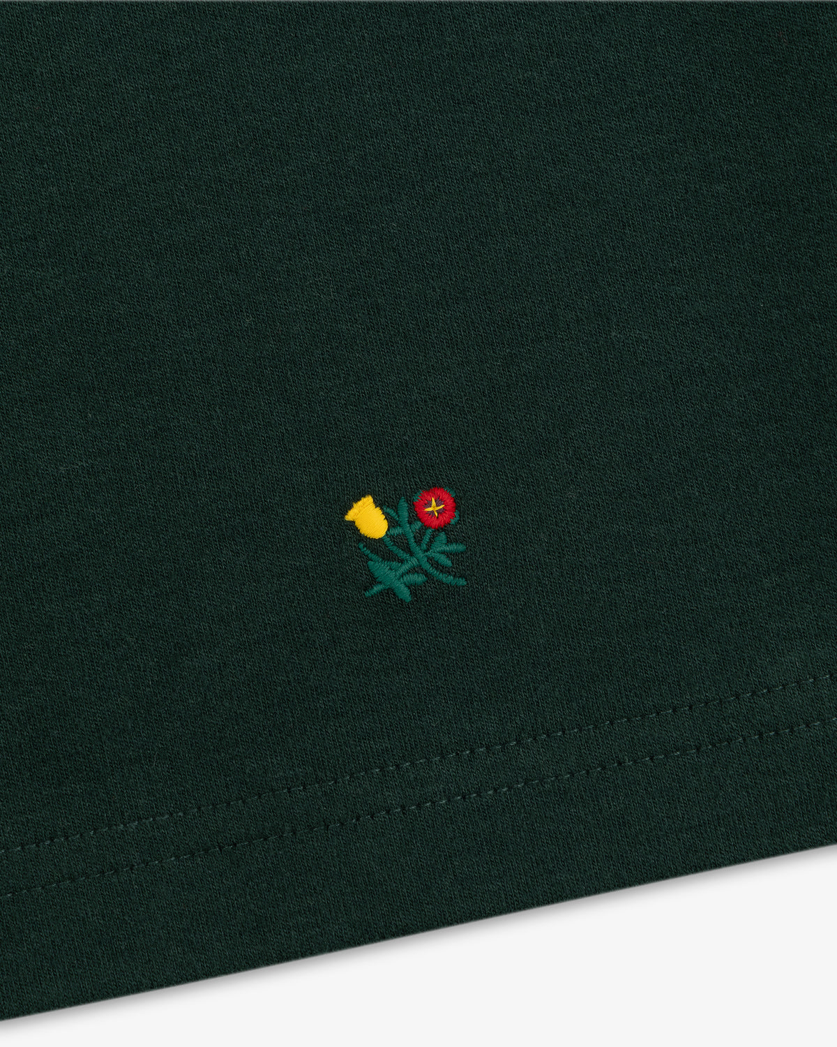 Heavyweight Crest Mockneck Tee in dark green with a small yellow and red embroidered flower design.
