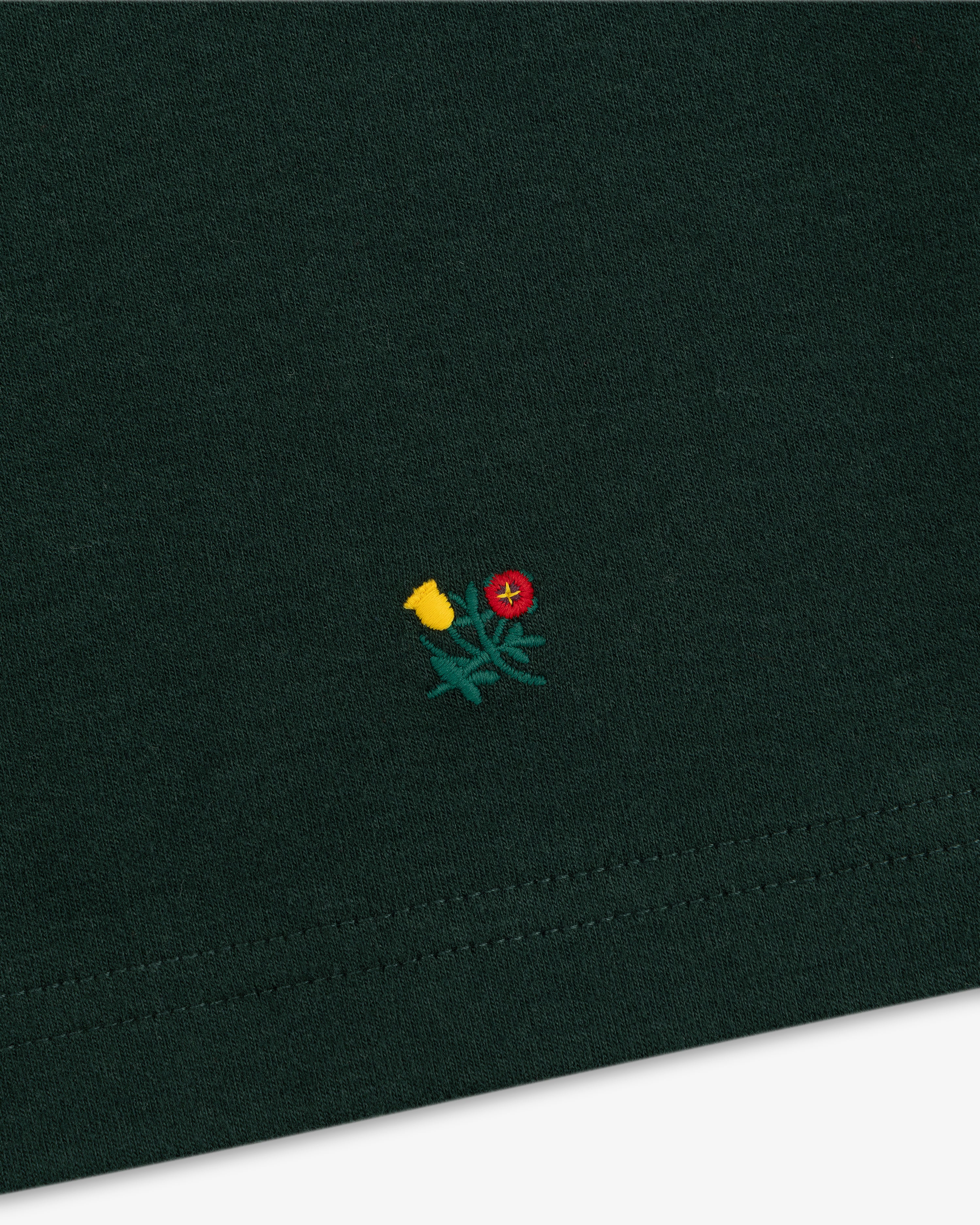 Heavyweight Crest Mockneck Tee in dark green with a small yellow and red embroidered flower design.