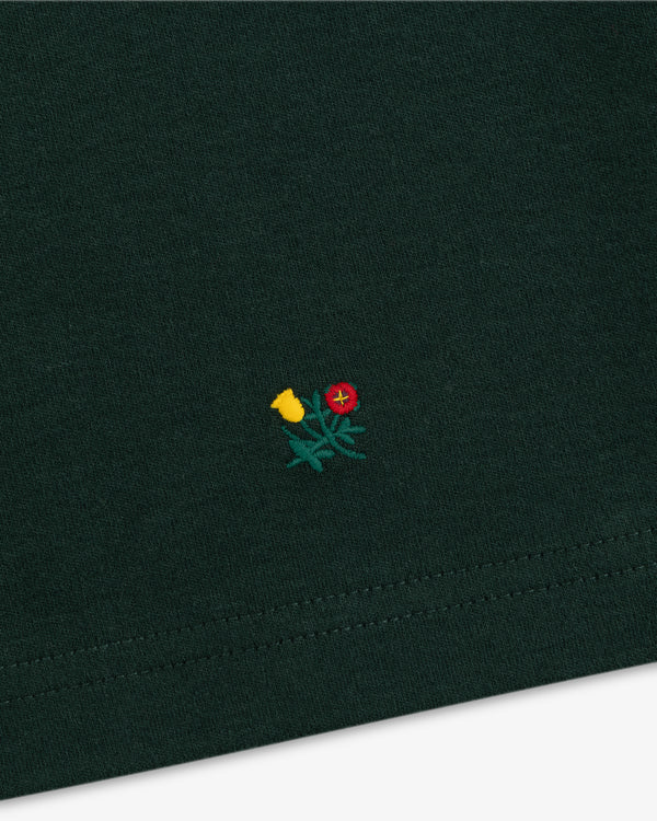 Heavyweight Crest Mockneck Tee in dark green with a small yellow and red embroidered flower design.