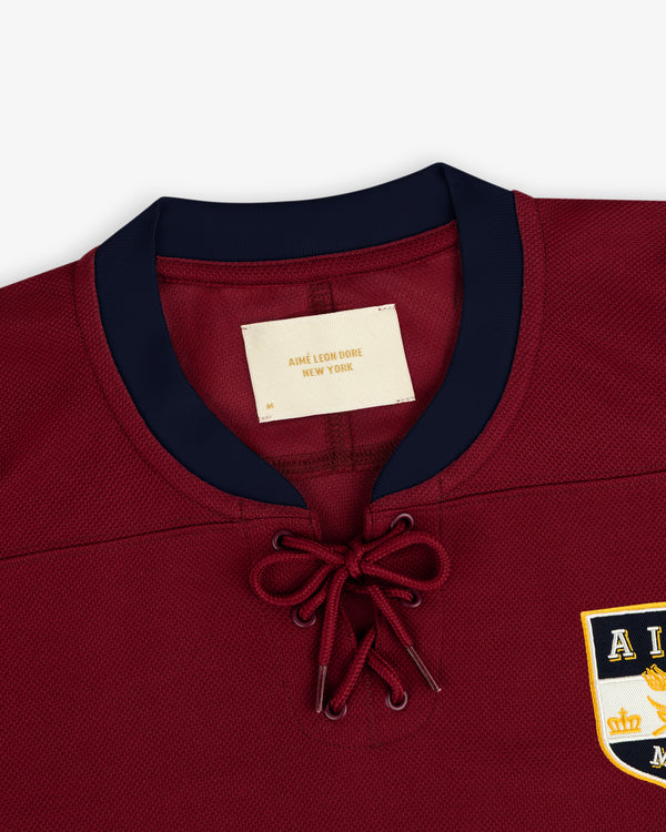 Team Aimé Hockey Jersey in maroon with a lace-up collar, navy blue trim, and a branded chest patch.